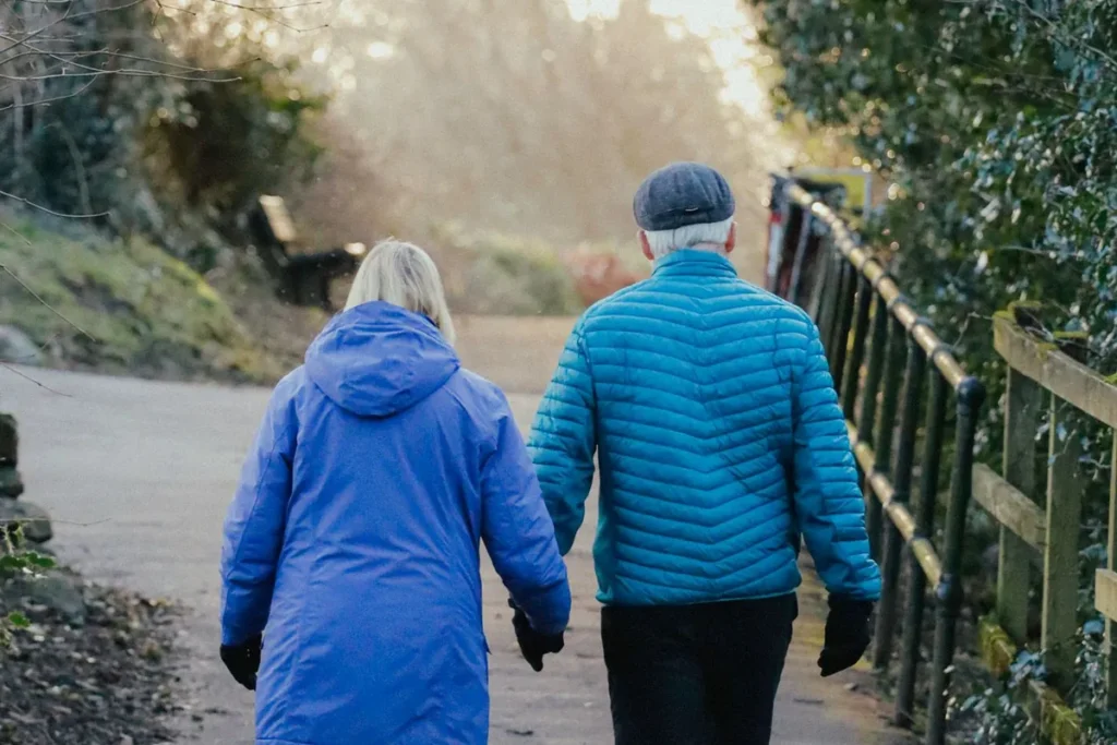 Older couple in blue jackets walking together along a park path
