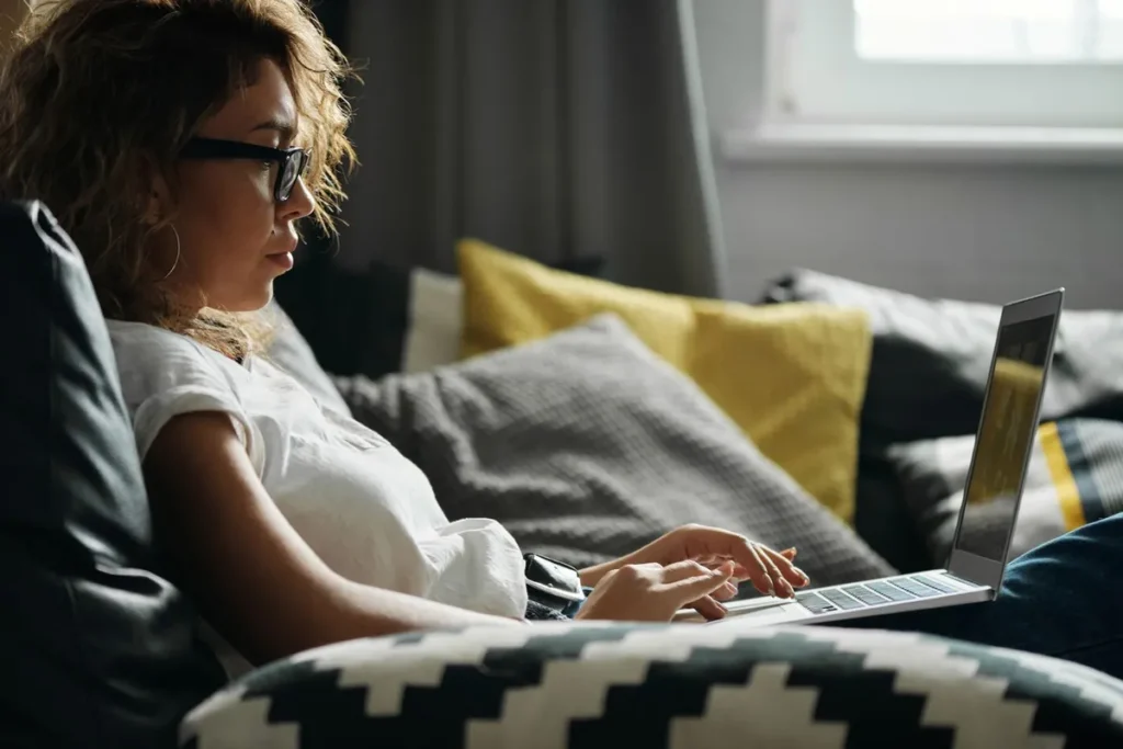 Woman with glasses using a laptop on a sofa