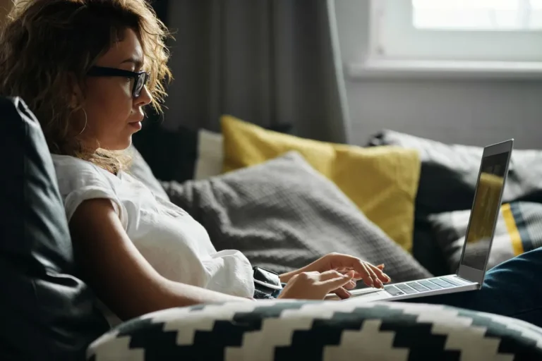 Woman with glasses using a laptop on a sofa