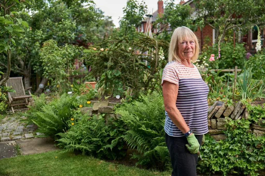 Smiling older woman standing in a green garden wearing gardening gloves