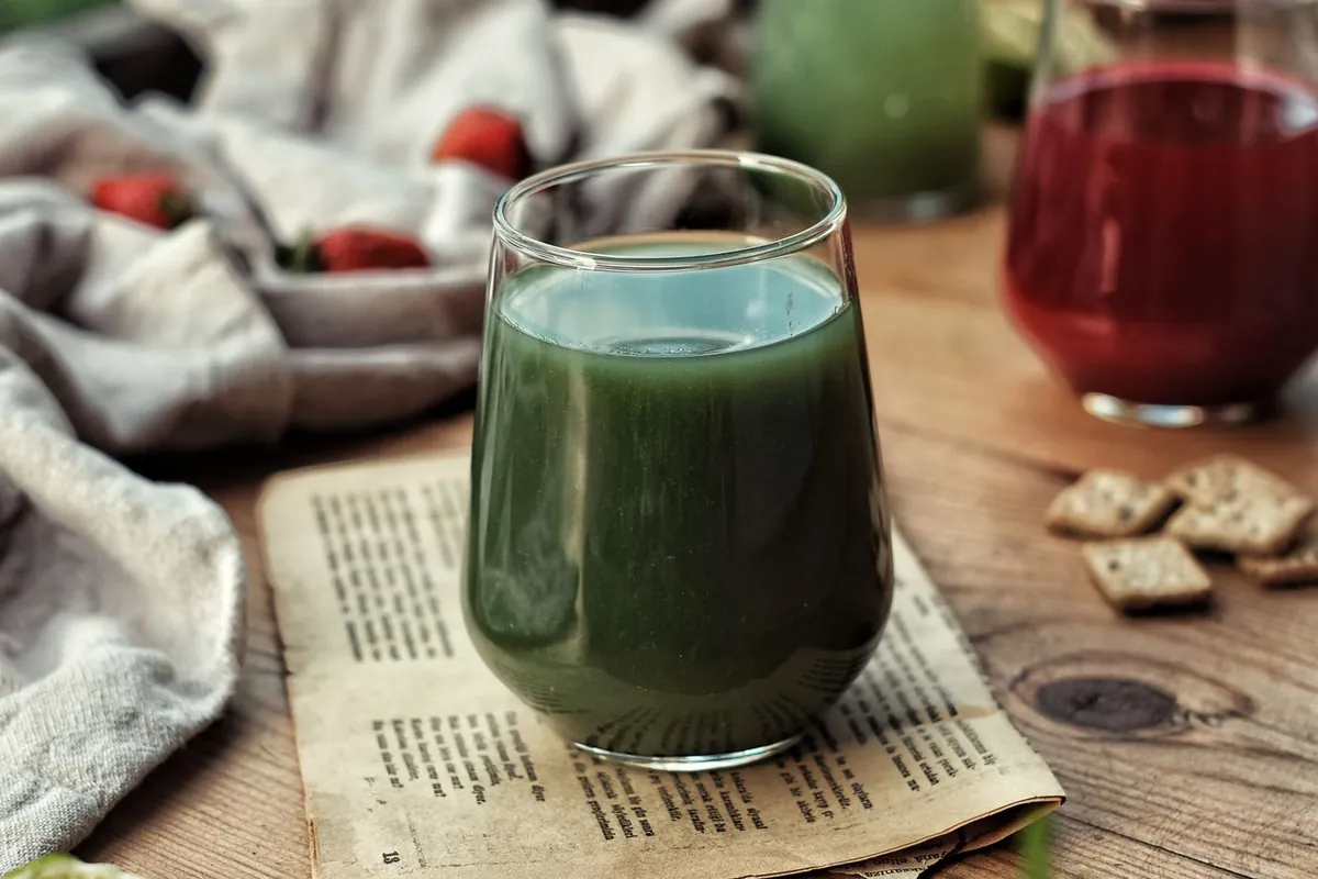 Glass of green juice on a wooden table with a red drink and fresh herbs