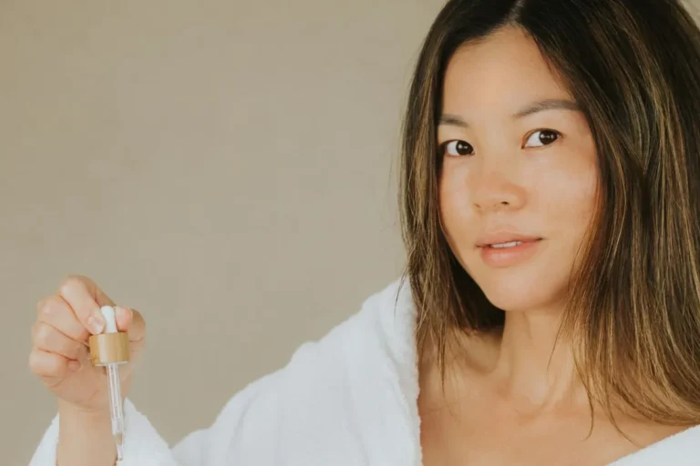 Woman in a white robe holding a serum dropper bottle