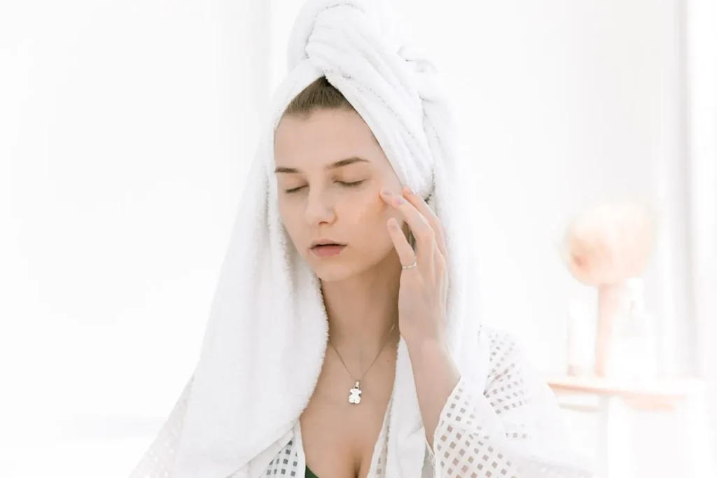 Woman with a towel wrapped around her hair, touching her cheek after cleansing