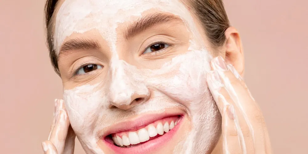 Smiling woman washing her face with cleansing foam