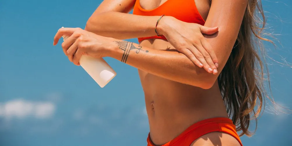 Woman applying sun protection to her arm under a clear blue sky