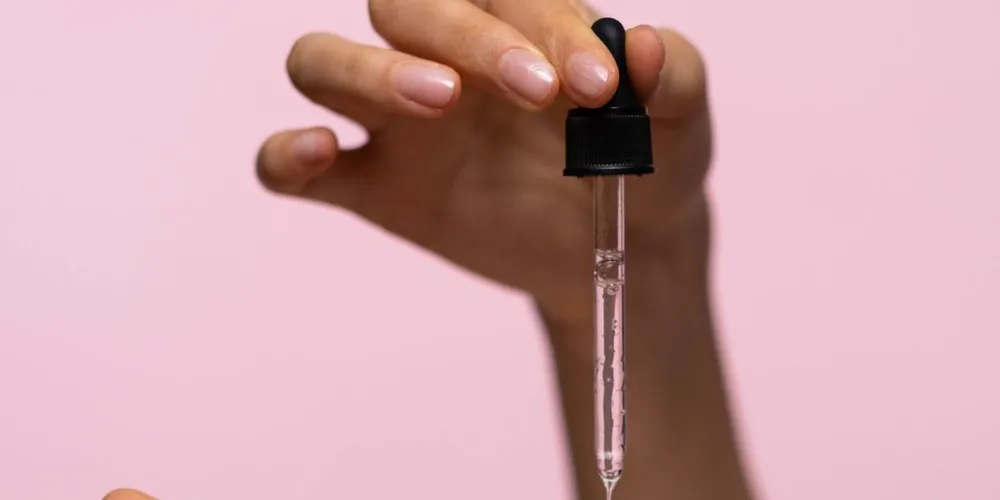 Hand holding a serum dropper above an open palm on a pink background