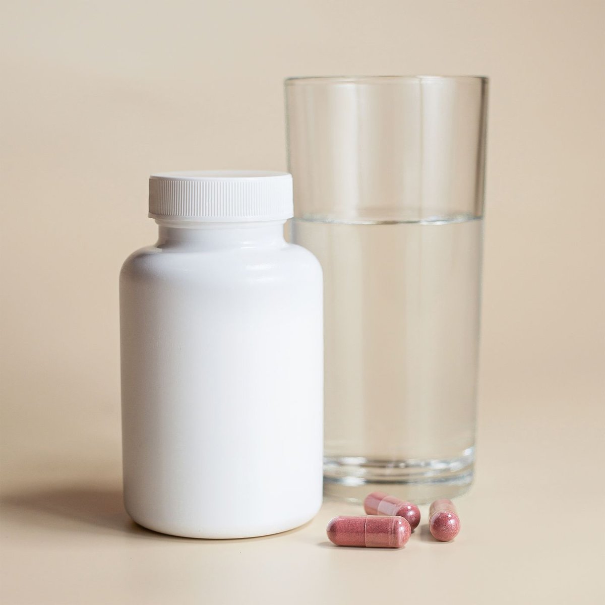 White supplement bottle beside a glass of water and two capsules